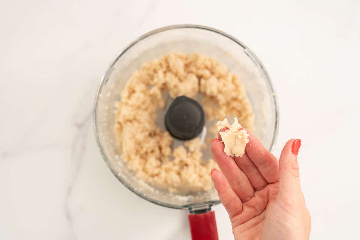 Women's hand holding coconut ball mixture in their hand, the mux can be squashed like play dough.