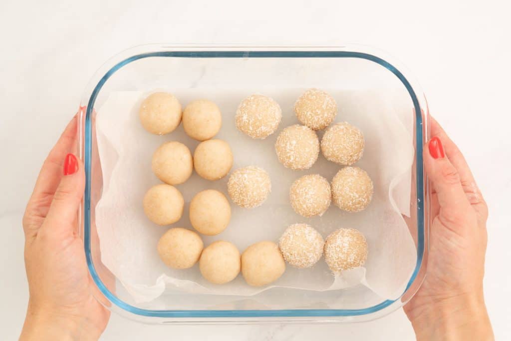 Coconut snow balls in a baking paper lined glass container ready to go into the fridge.