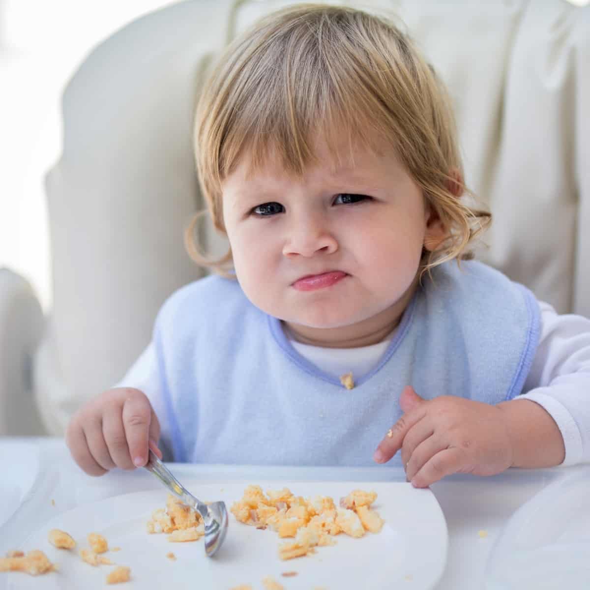 A toddler sitting in a high chair with a plate of scrambled eggs.