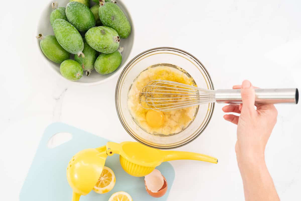Feijoa flesh, lemon rind, egg, oil and vanilla being whisked in a glass bowl.