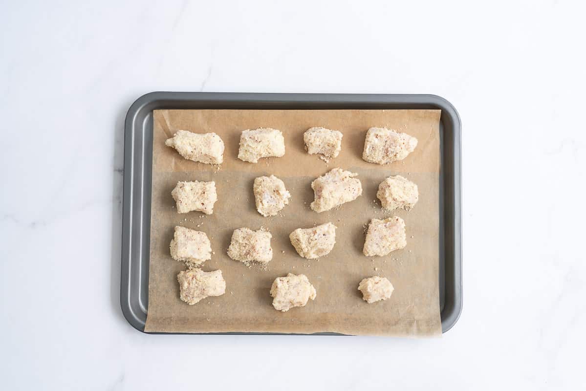 almond crusted chicken nuggets on a baking paper lined oven tray.