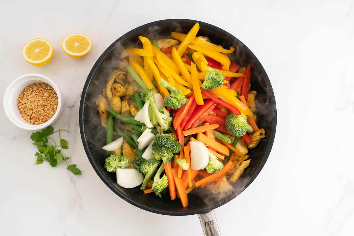 A fry pan full of sliced vegetables and sealed chicken.
