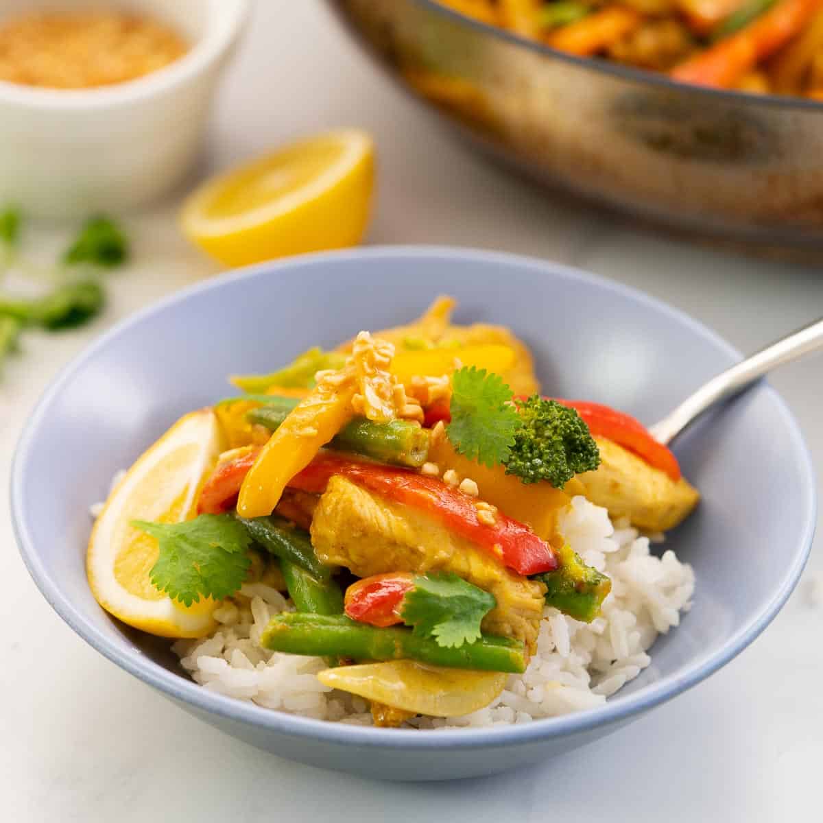 A blue bowl of chicken and vegetables with a peanut satay sauce on rice.