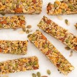 Energy bars on white crumpled baking paper surrounded by scattered nuts and seeds.