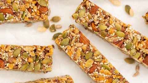 Energy bars on white crumpled baking paper surrounded by scattered nuts and seeds.