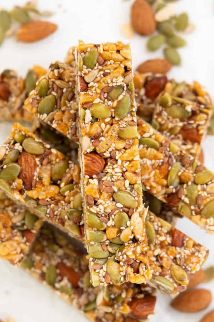 An energy bar full of seeds and nuts sitting on a stack of energy bars.