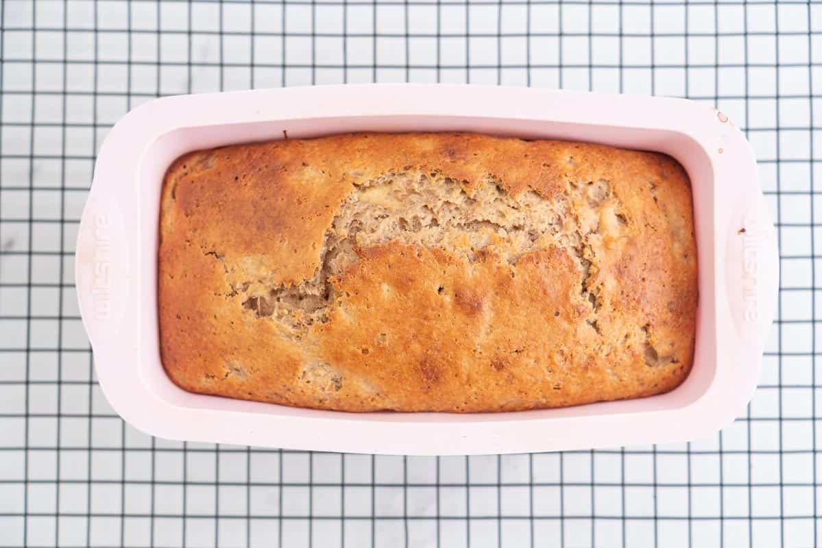 Golden baked loaf in a pink loaf tin on a cooling rack.
