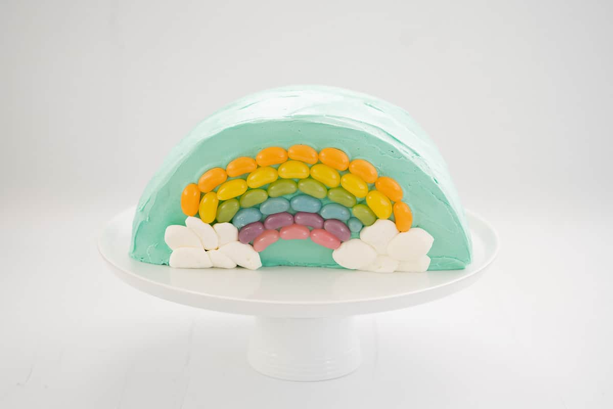 Half round cake standing on a white serving platter decorated with a rainbow of jellybeans.