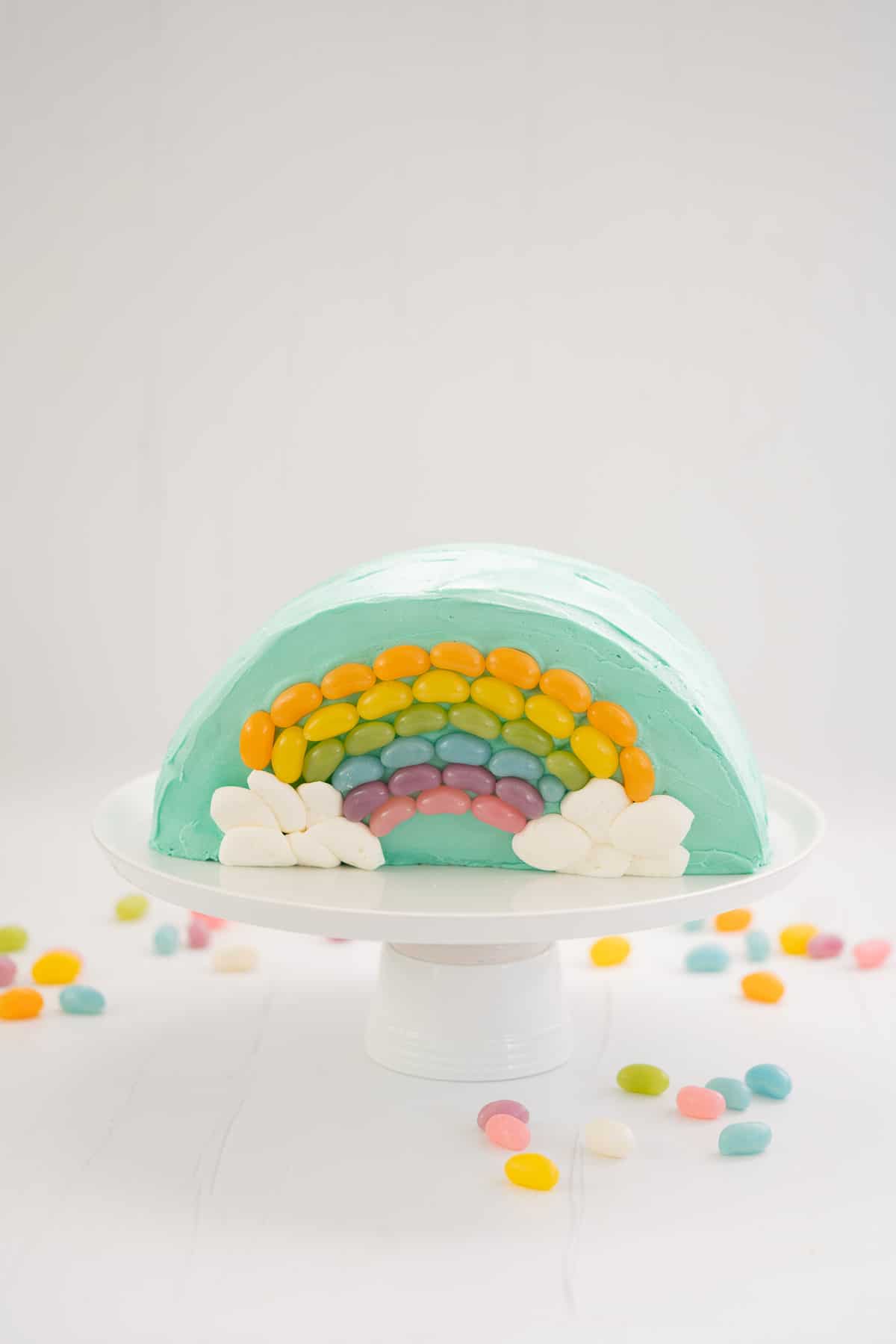 Rainbow Cake: Half round cake standing on a white serving platter decorated with a rainbow of jellybeans.