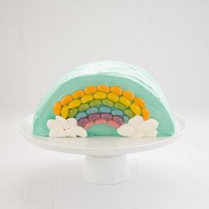 Rainbow Cake: Half round cake standing on a white serving platter decorated with a rainbow of jellybeans.