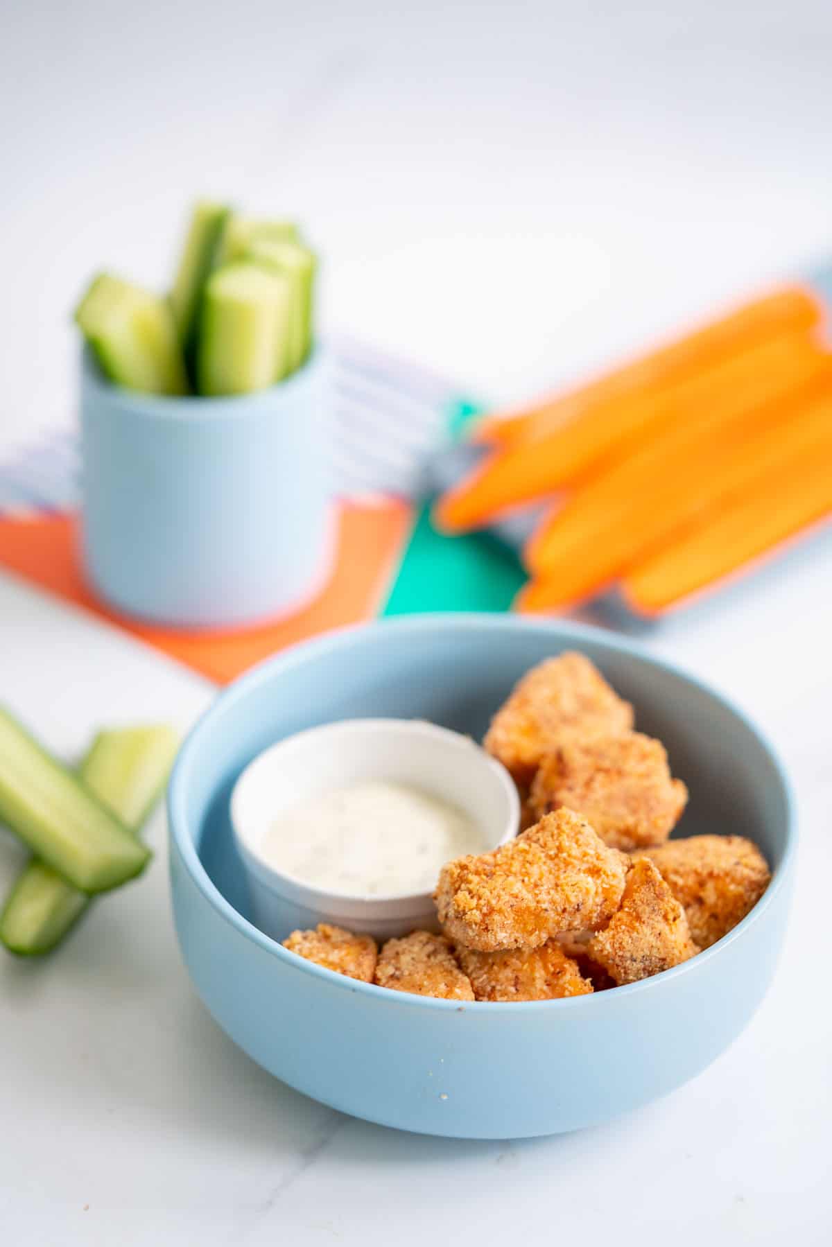 A blue bowl filled with salmon nuggets, cucumber and carrot sticks in the background.
