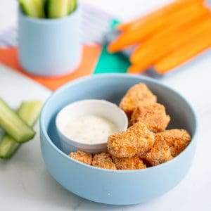 A blue bowl filled with salmon nuggets, cucumber and carrot sticks in the background.