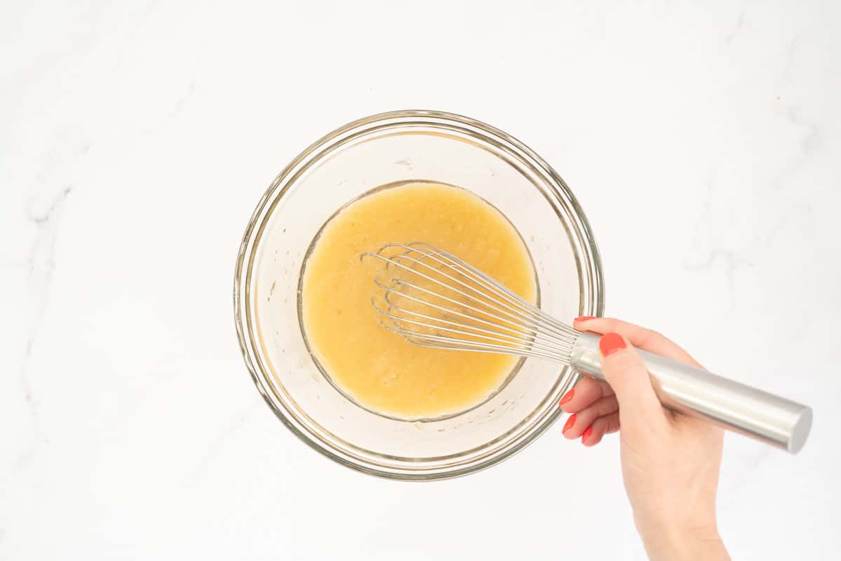 A medium sized glass mixing bowl containing apple sauce and oil being mixed.