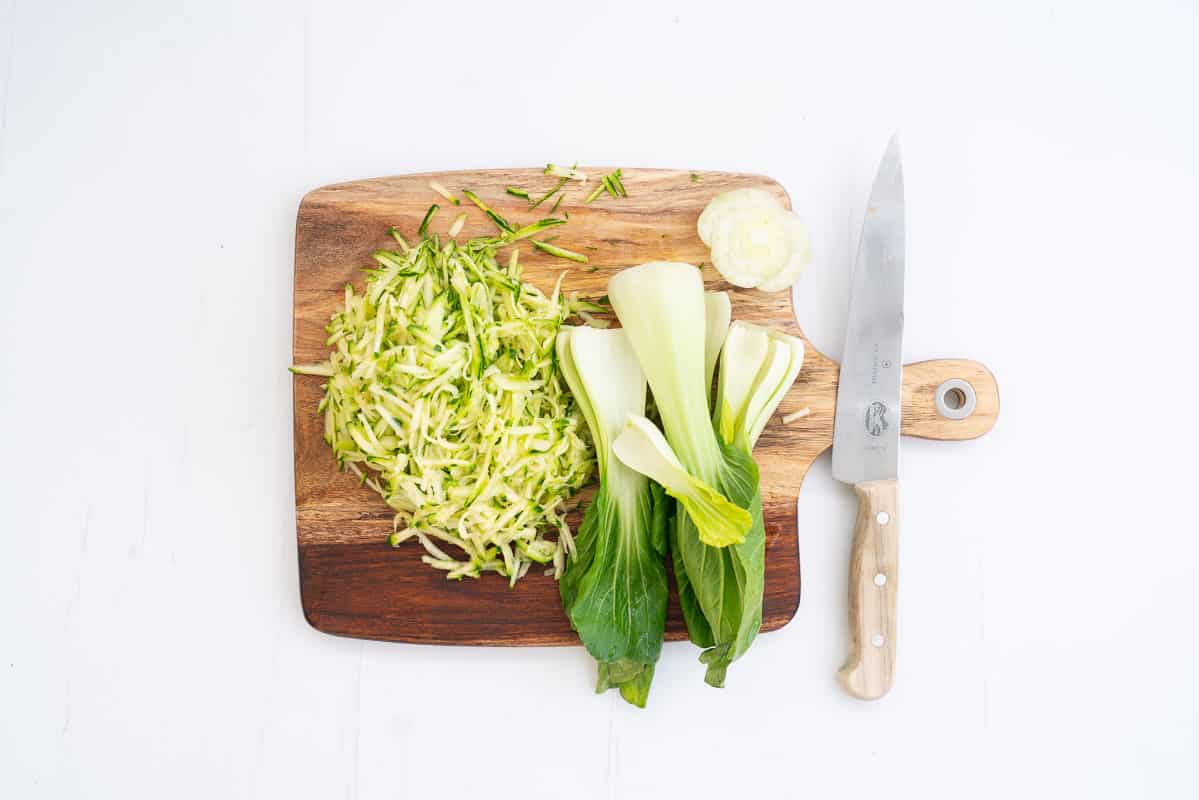 Grated zucchini and bok choy leaves on a wooden chopping board.