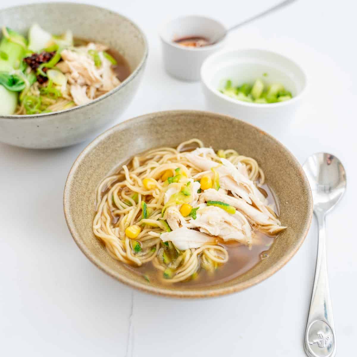 A grey ceramic bowl of chicken noodle soup. chicken, noodles and corn visible..