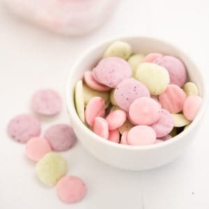 a small white bowl of baby yogurt melts in 3 colours, pale pink, lavender and pale green.