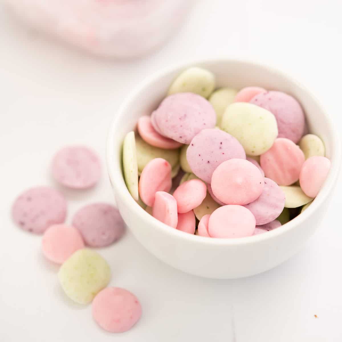 a small white bowl of baby yogurt melts in 3 colours, pale pink, lavender and pale green.