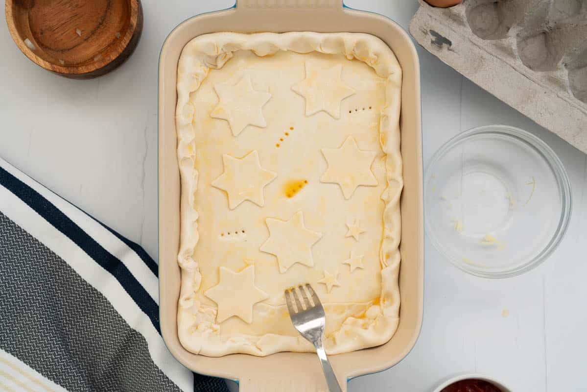 The top of a pie being pierced by a fork to create air holes.