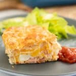A slice of bacon and egg pie on a blue plate, with tomato relish and salad.