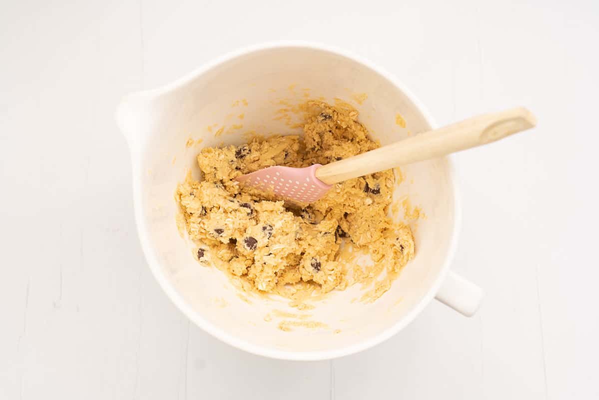 Chocolate chip condensed milk cookie dough in a mixing bowl with wooden spoon.