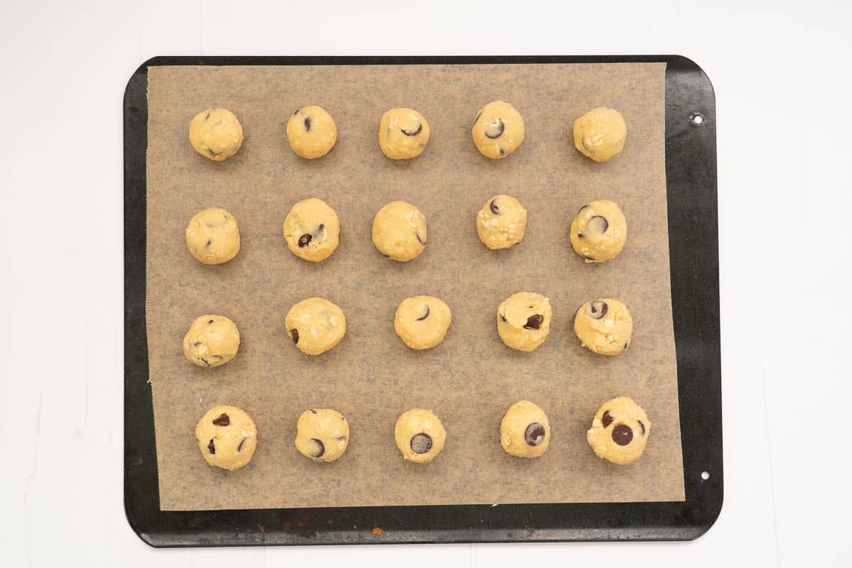 24 balls of cookie dough on a baking paper lined tray.