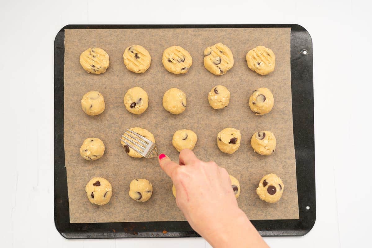 Women's hand pressing balls of cookie dough using a fork
