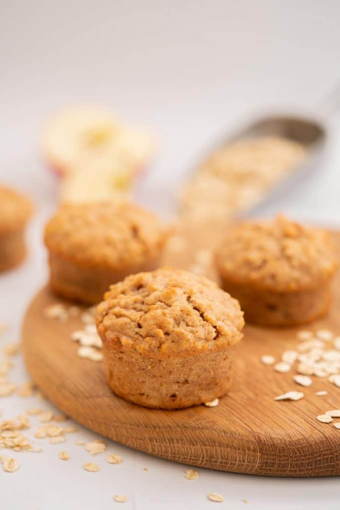 Apple muffins on a wooden chopping board scattered with rolled oats.