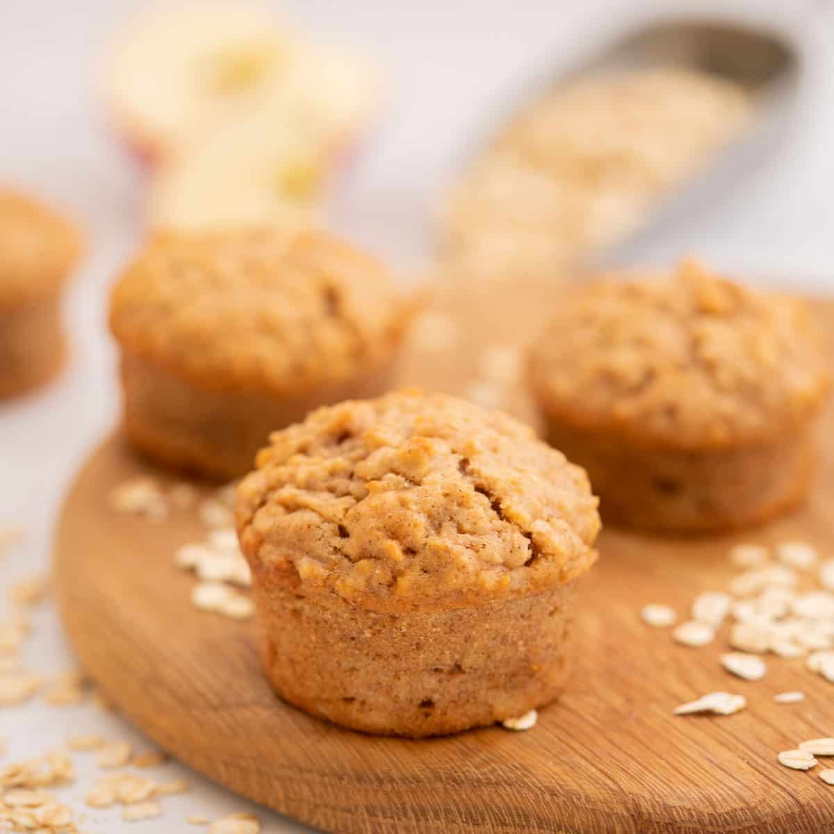 Apple muffins on a wooden chopping board scattered with rolled oats.