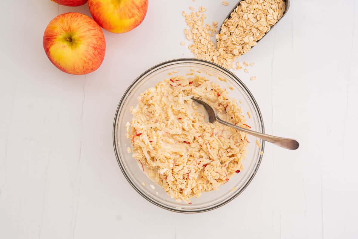 Grated apple and rolled oats soaking in milk in a glass mixing bowl