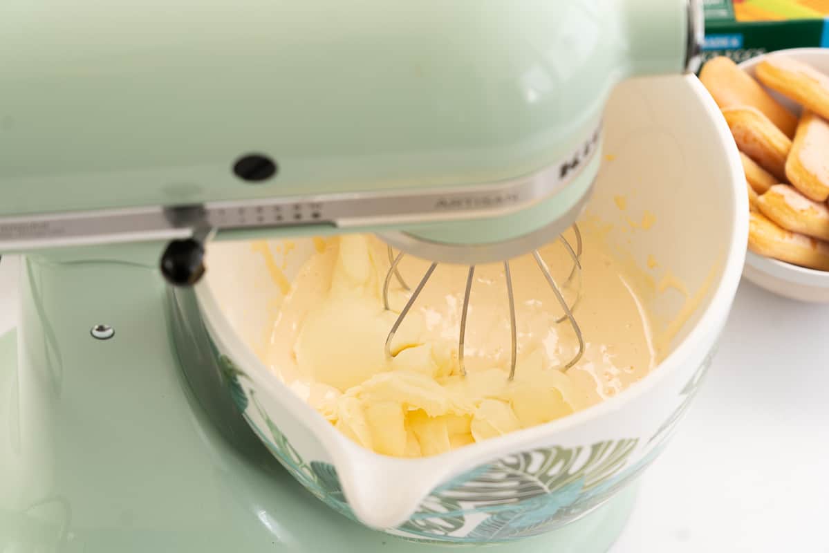 Pale green stand mixer with mascarpone and a thick custard based ready to be whipped in a white ceramix mixing bowl.
