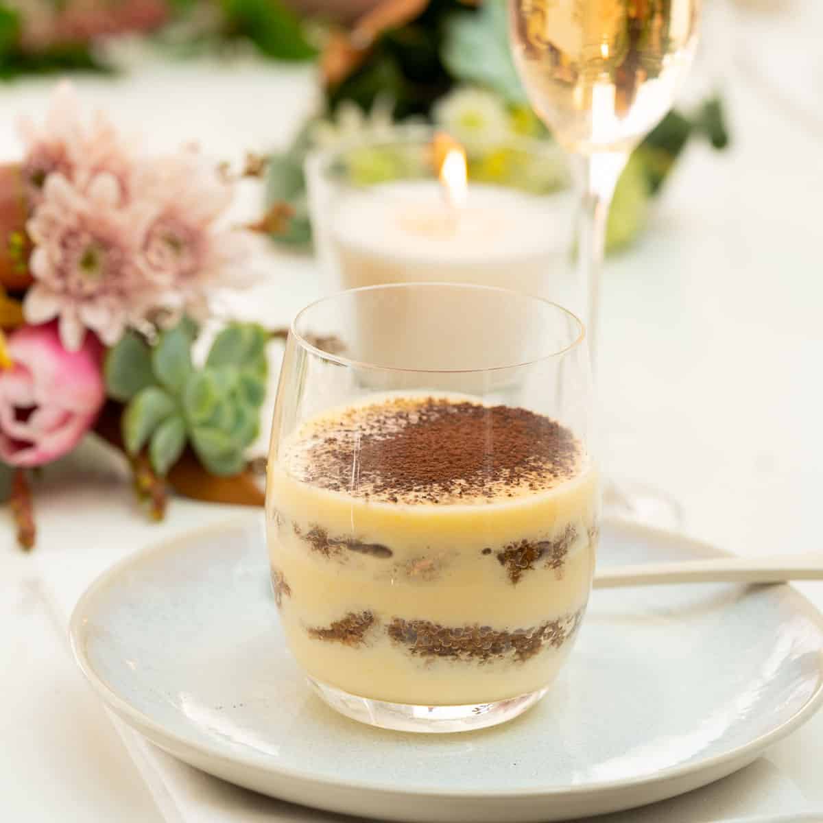 Tiramisu served in a glass, a candle, and flowers in the background.
