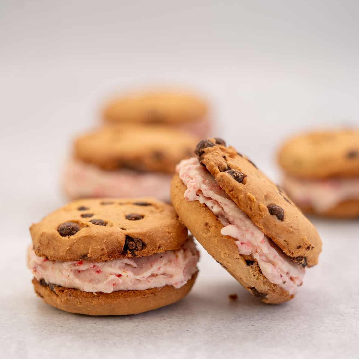 Chocolate Chip Cookie and Strawberry Ice Cream Sandwiches laid out on a bench top.