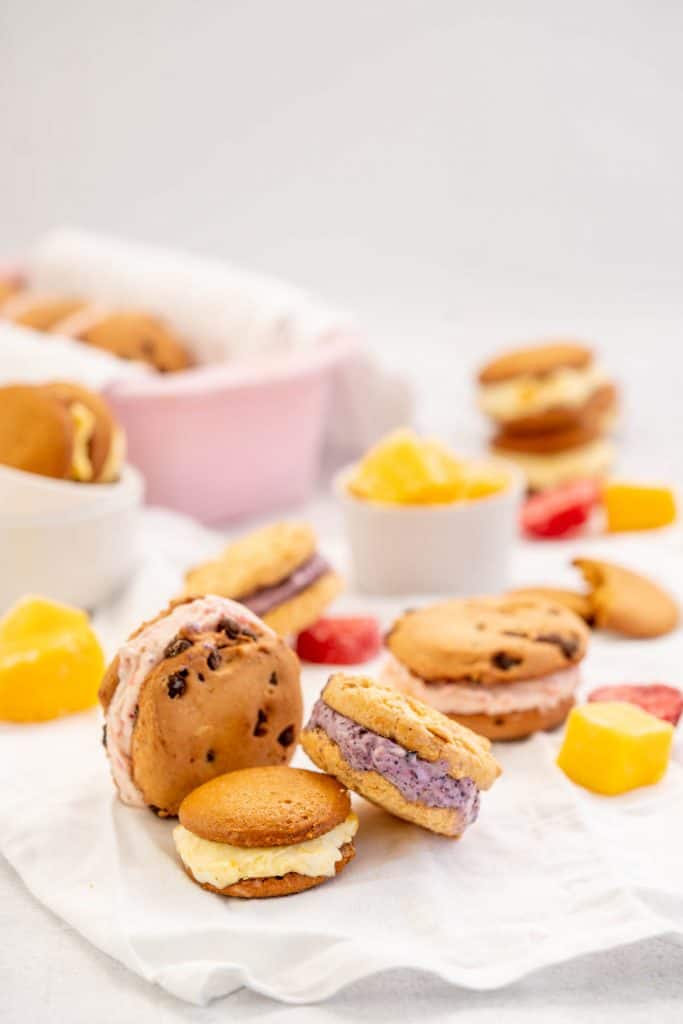 3 diffferent flavoured ice cream cookie sandwiches with frozen fruit pieces.