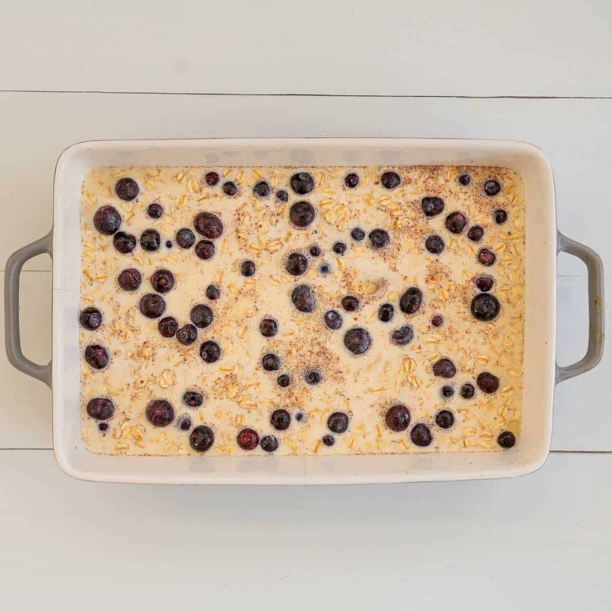 A baking dish of rolled oats, milk, eggs and blueberries ready to be baked in the oven.