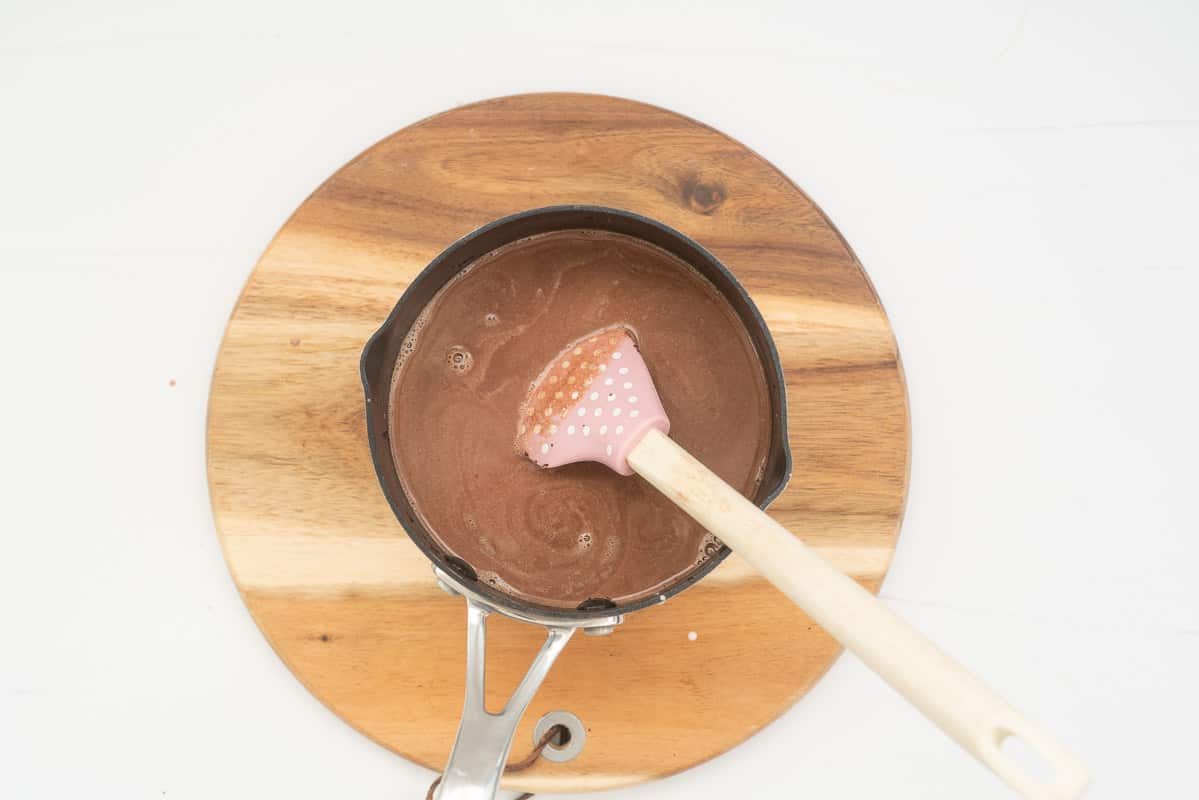 A sauce pan of hot chocolate being sired with a pink spatula.