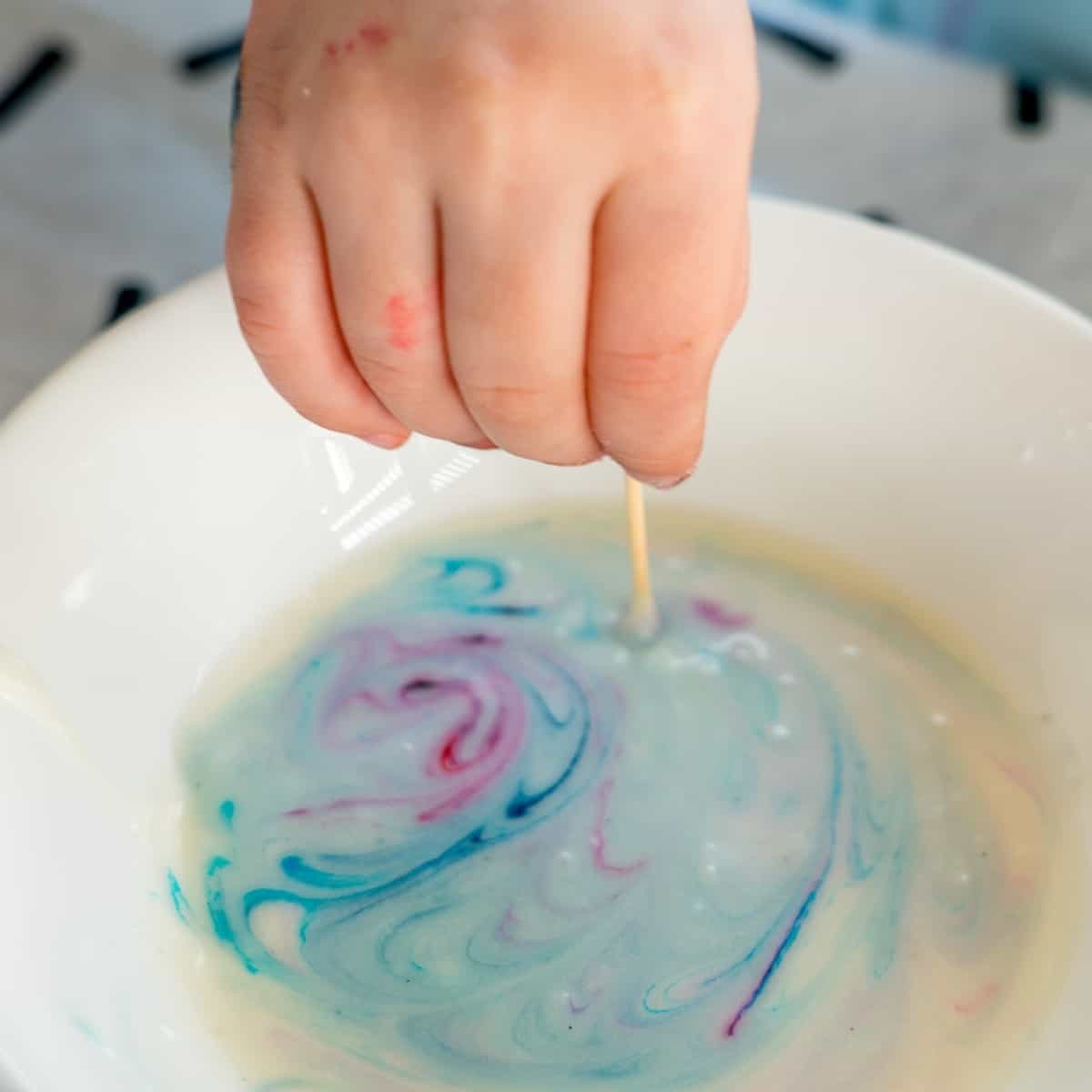 A child's hand swirling food colouring through cookie glaze using a tooth pick.