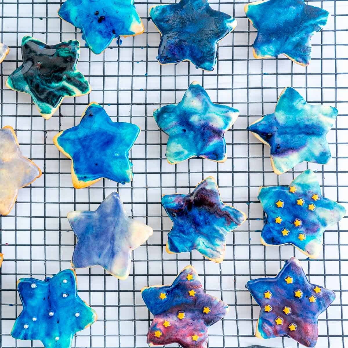 14 star shaped galaxy iced cookies on a wire rack.