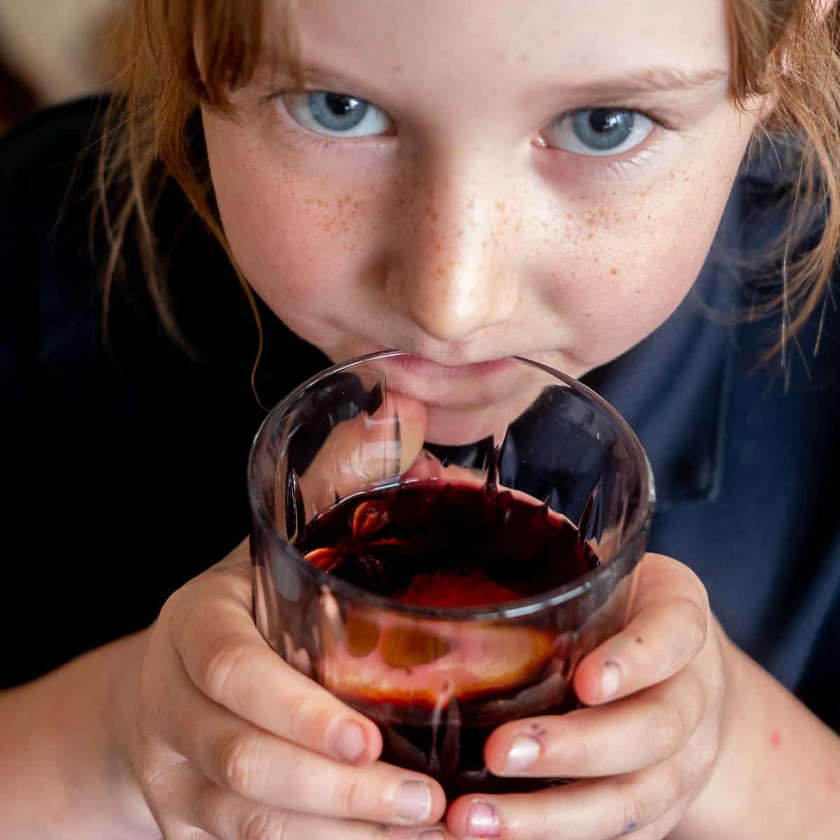 A blue eyed girl taking a sip from a glass of non-alcoholic mulled wine.