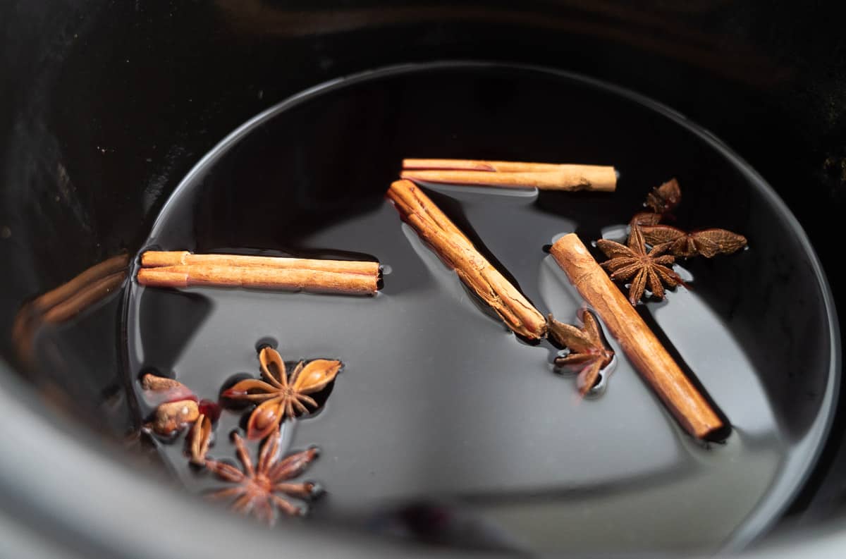 Dark grape juice in a slow cooker with cinnamon quills and star anise floating on the surface.