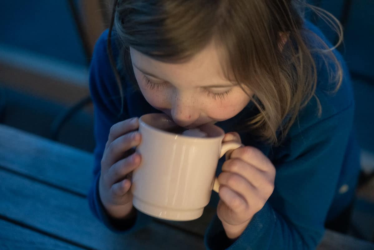A young girl drinking hot chocolate from a pink mug at night time.