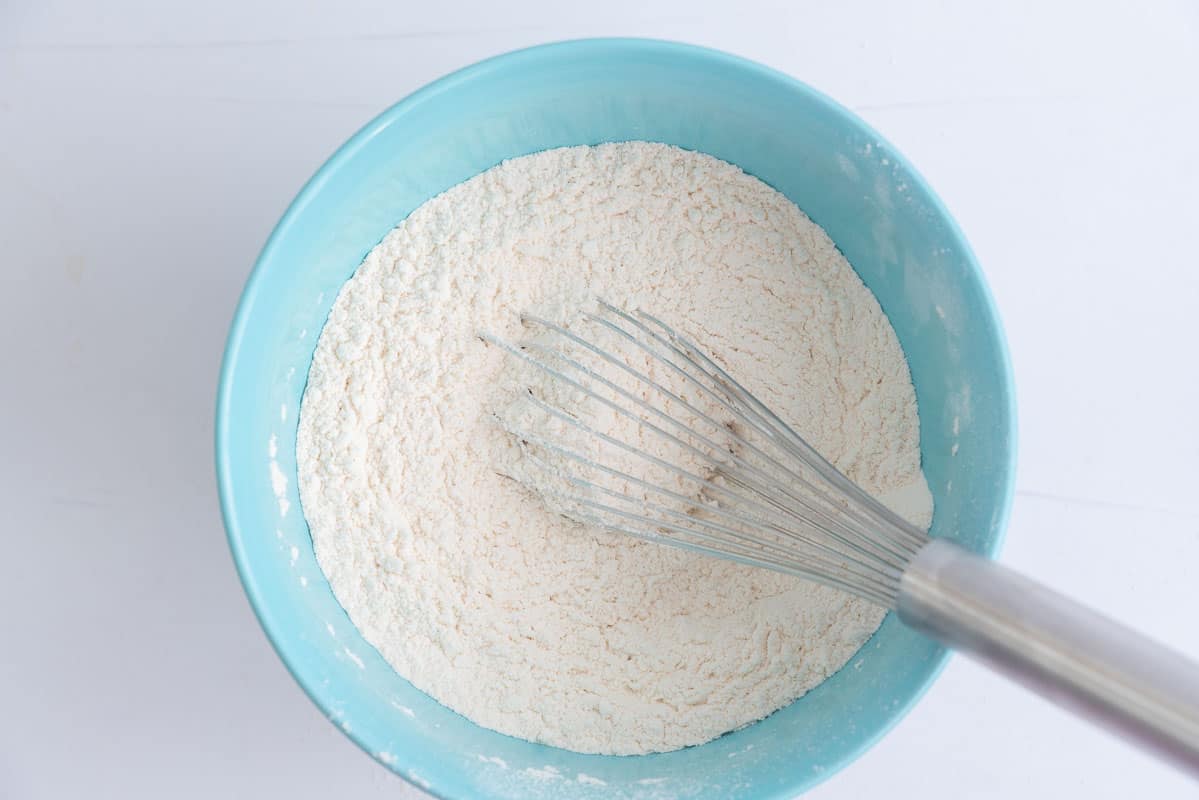 Flour in a light blue plastic mixing bowl with a whisk.