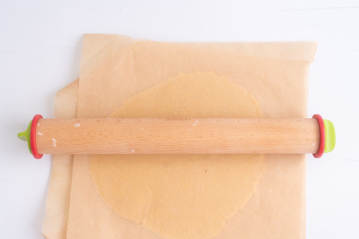 Cookie dough sandwiched between two sheets of baking paper rolled out with a rolling pin.