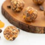 An apricot ball on a white bench top with a wooden tray of more apricot balls in the background.