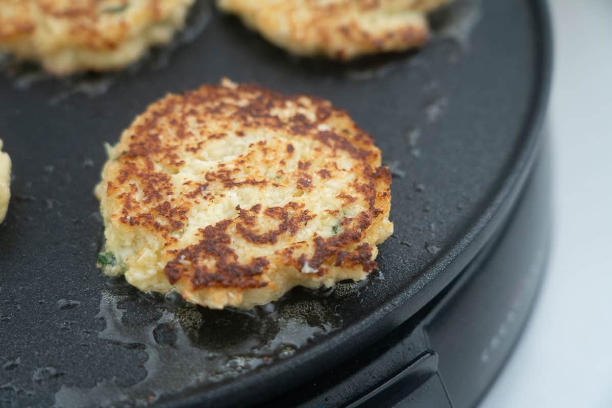 A golden brown fritter cooking on a greased skillet.