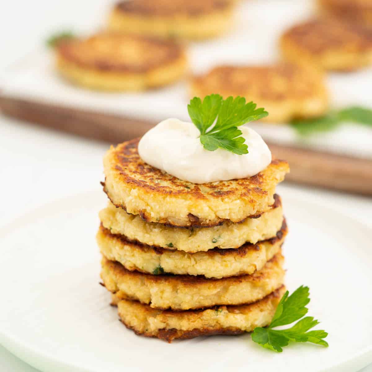 A stack of 5 cauliflower fritters topped with aioli and parsley.
