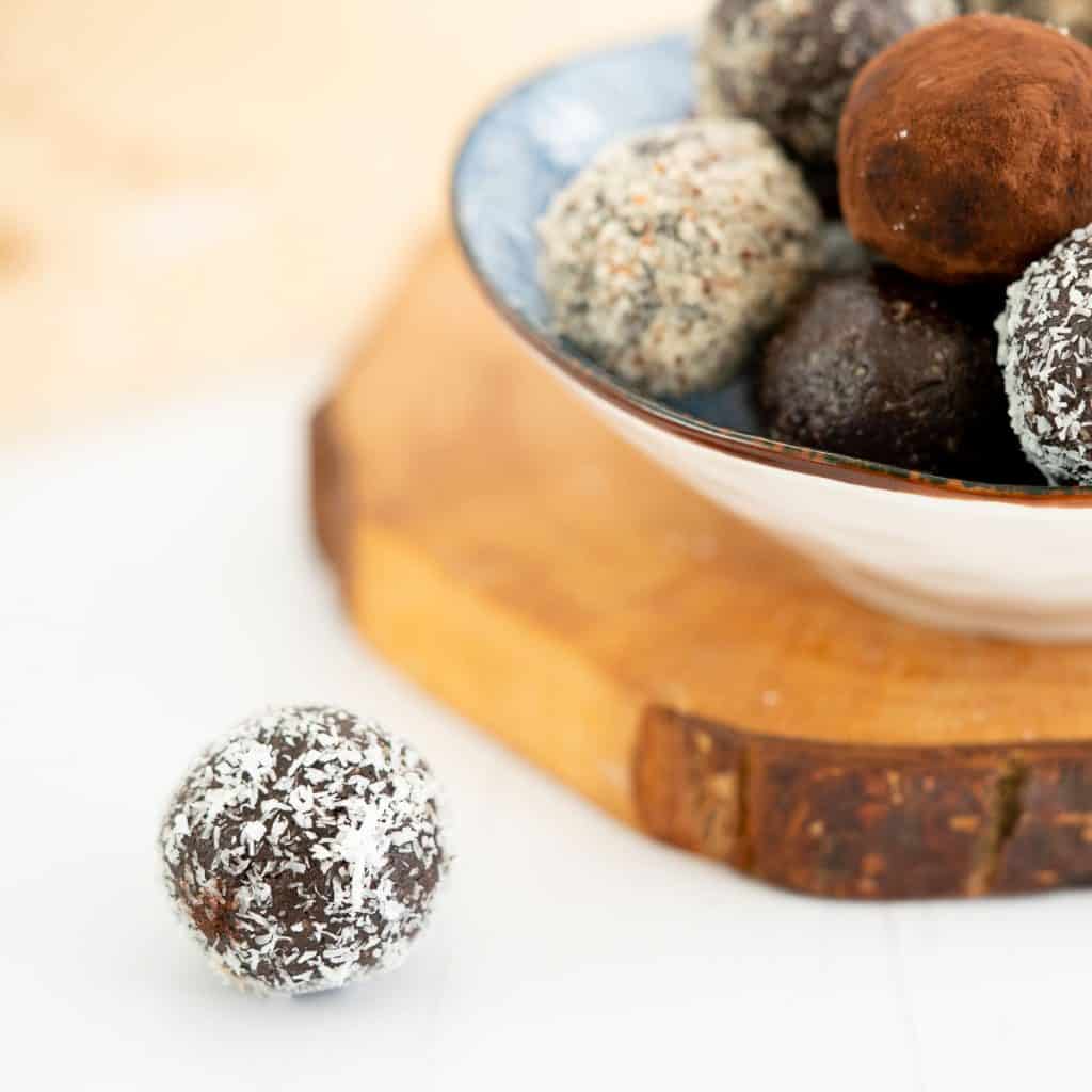 A coconut covered chocolate ball sitting on a white bench top.