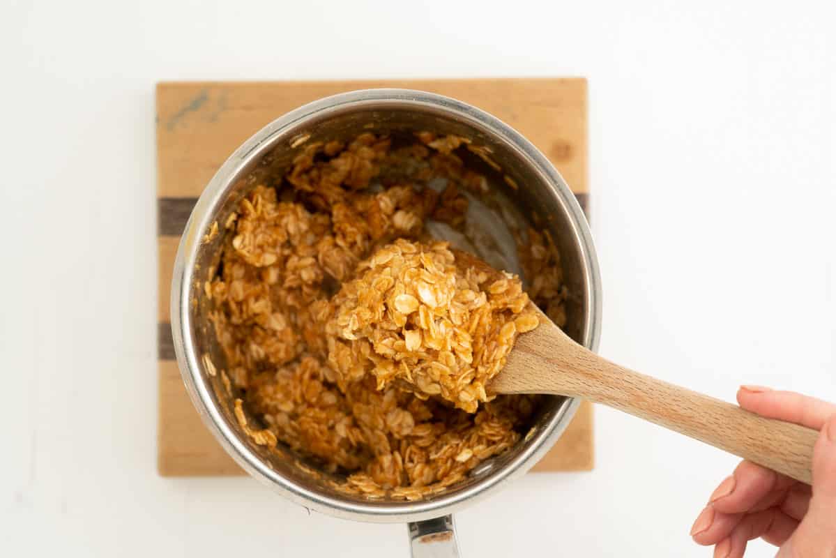 A wooden spoon stirring rolled oats through peanut butter caramel.