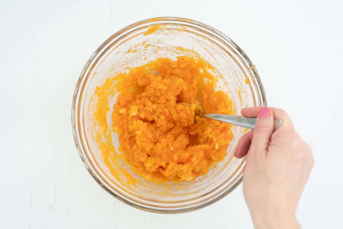 A glass mixing bowl filled with mashed sweet potato and banana.
