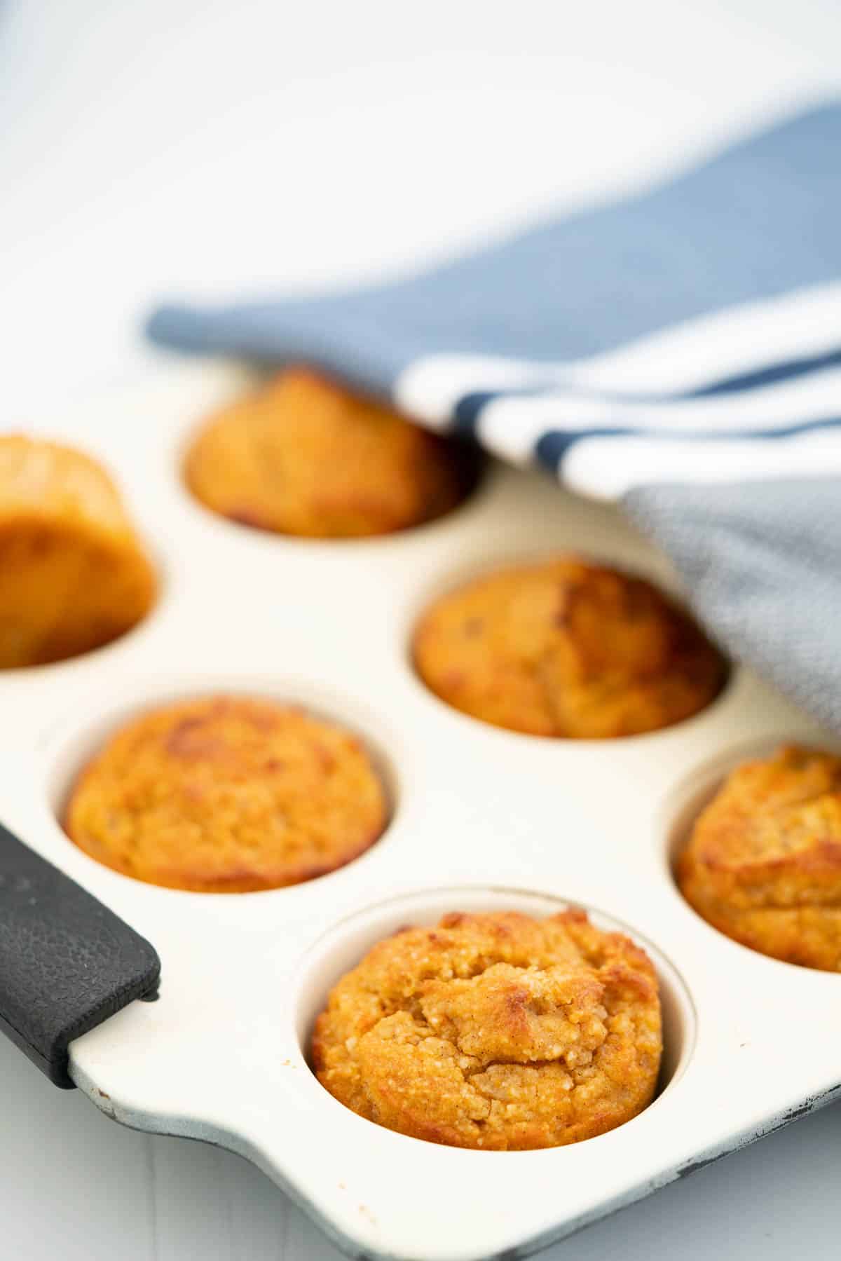Cooked sweet potato muffins in a cream muffin tray draped with a blue striped cloth.