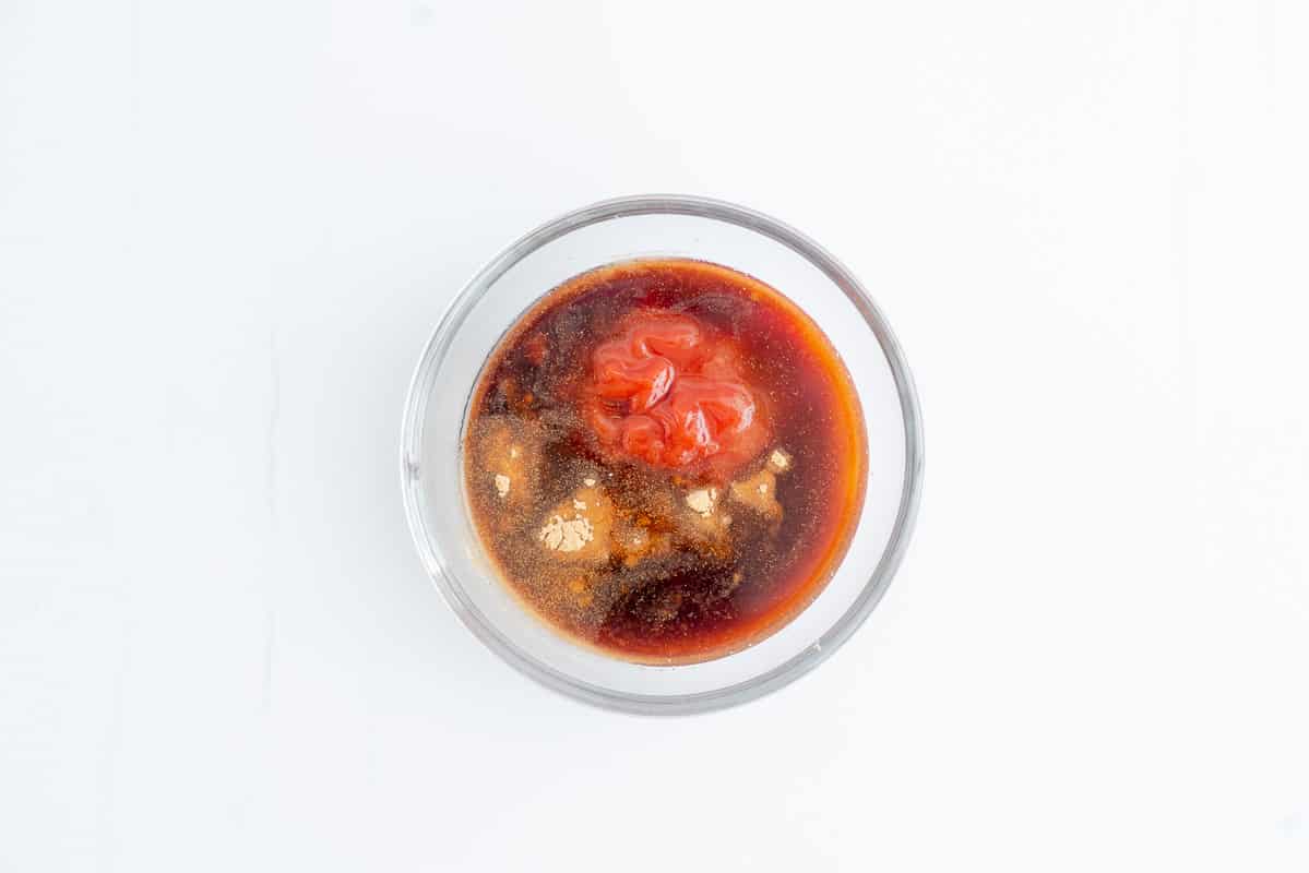 A small glass mixing bowl containing tomato sauce, brown sugar, soy sauce and vinegar.